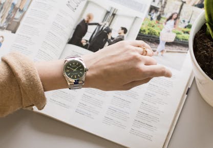 Rolex Oyster Perpetual 40mm watch worn on a 6 inch woman’s wrist while reading a magazine