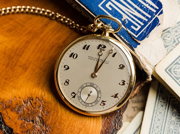 Vintage Patek Philippe pocket watch with gold case and chain resting on a wooden surface.
