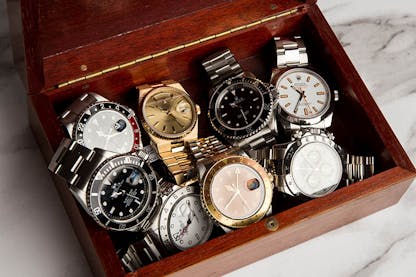 Collection of vintage and modern Rolex watch models including Submariner, GMT-Master, and Day-Date in a wooden box – highlighting Rolex history and model evolution