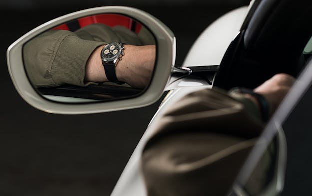 Vintage Rolex Daytona chronograph reflected in car side mirror, showcasing its motorsport heritage